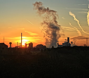 Industrial factory smokestacks silhouetted against sunset sky