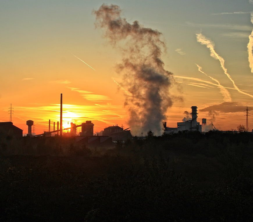 Industrial factory smokestacks silhouetted against sunset sky