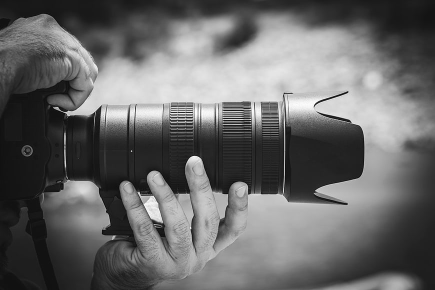 Close-up of hands holding professional camera with telephoto lens
