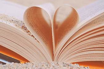 Open book pages folded into heart shape on sand