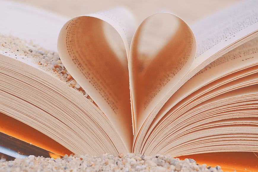 Open book pages folded into heart shape on sand
