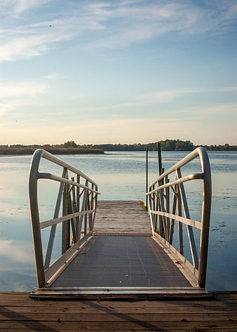 Wooden Dock Extending Into Calm Lake At Sunset