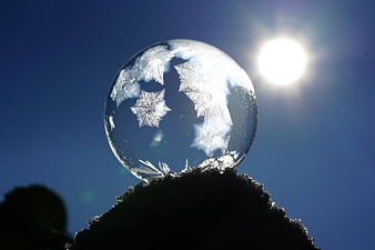 Frozen soap bubble with ice crystals against blue sky