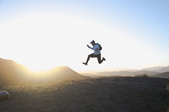 Man jumping in mid-air on mountain peak at sunset