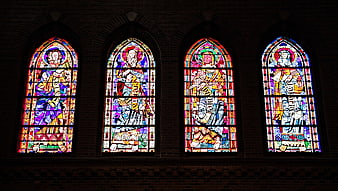 Four colorful stained glass windows in a brick church wall