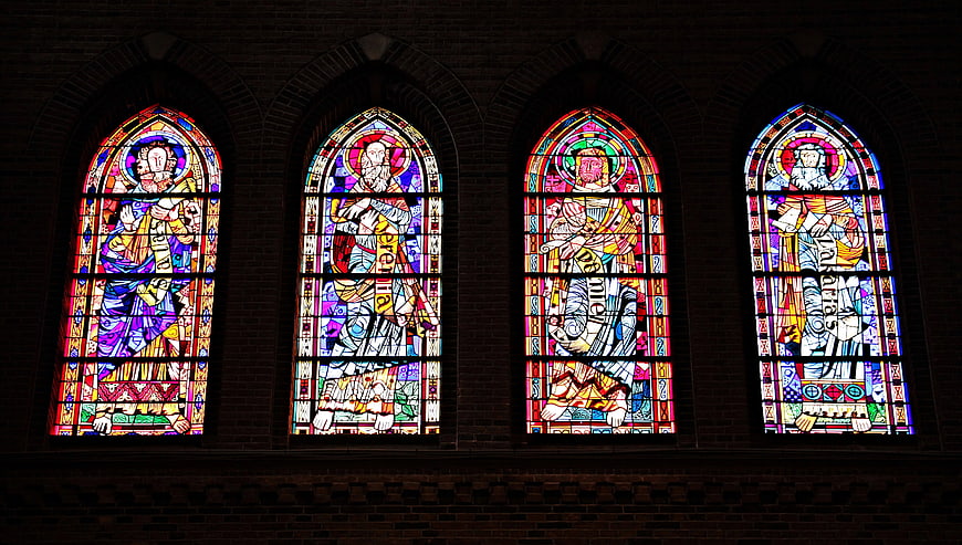 Four colorful stained glass windows in a brick church wall