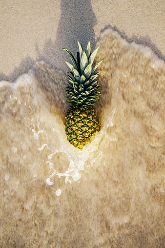 Top view of pineapple in ocean waves on sandy beach