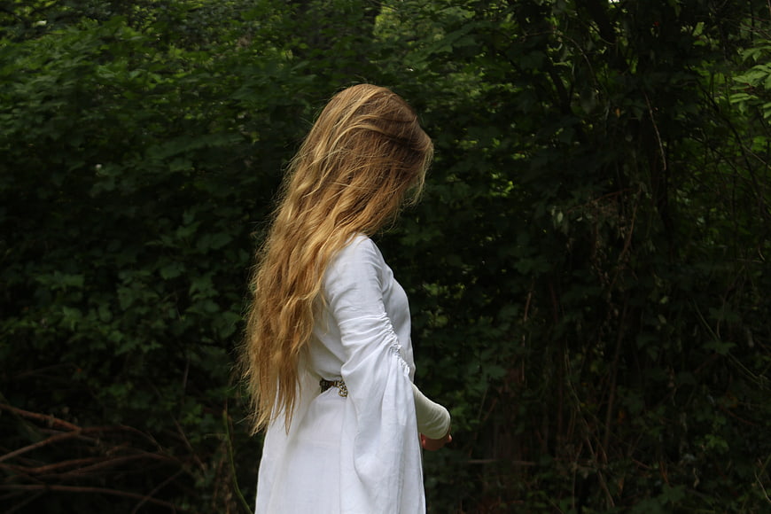 Woman in white dress with long blonde hair in dark forest