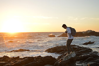 Man with Backpack Walking on Rocky Coast at Sunset