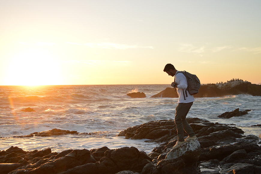Man with Backpack Walking on Rocky Coast at Sunset