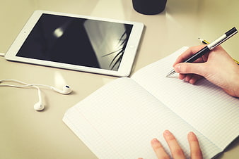 Student writing in notebook with tablet and headphones
