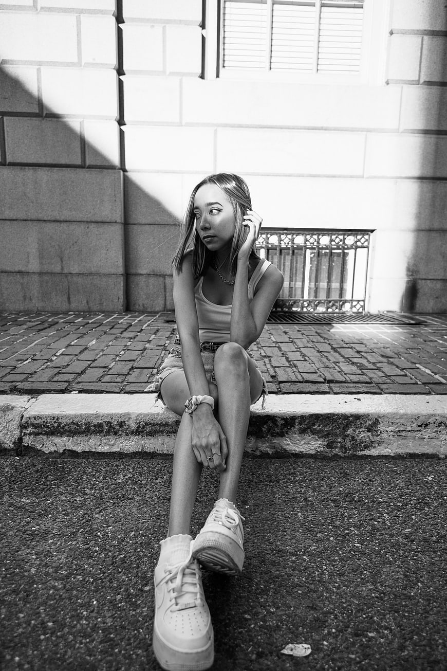 Black and white portrait of young woman sitting on urban curb