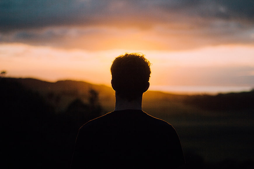 Silhouette of Man Watching Sunset Over Rolling Hills