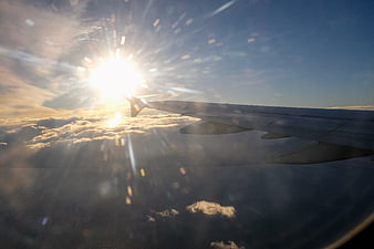 Airplane wing over clouds with bright sunburst