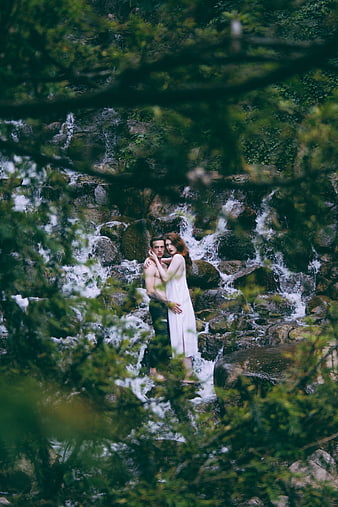 Romantic couple embracing in front of a forest waterfall