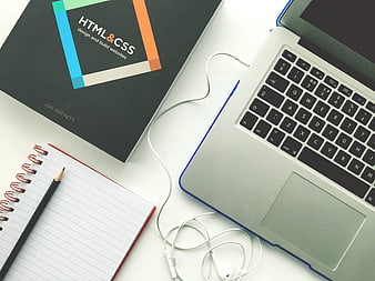 Flat lay of HTML CSS book, laptop, and notebook on white desk