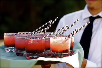 Waiter serving tray of red cocktails with striped straws