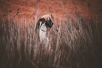 Hand holding camera in tall grass field