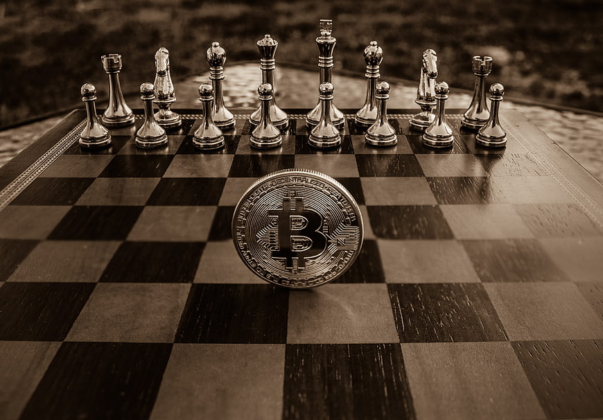 Bitcoin coin on chessboard with chess pieces in sepia tone