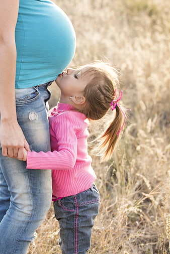 Toddler Girl Kissing Pregnant Mother's Belly in Field