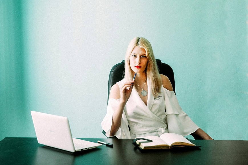 Blonde Businesswoman Sitting At Desk With Laptop And Notebook