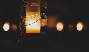 Close-up of glowing candle in textured glass with bokeh background