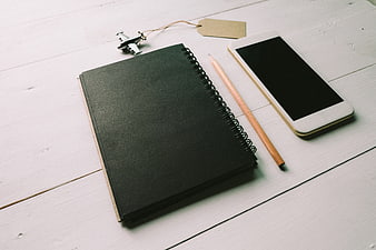 Minimalist workspace with black notebook, smartphone, and pencil on white wood
