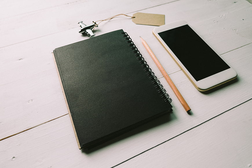 Minimalist workspace with black notebook, smartphone, and pencil on white wood