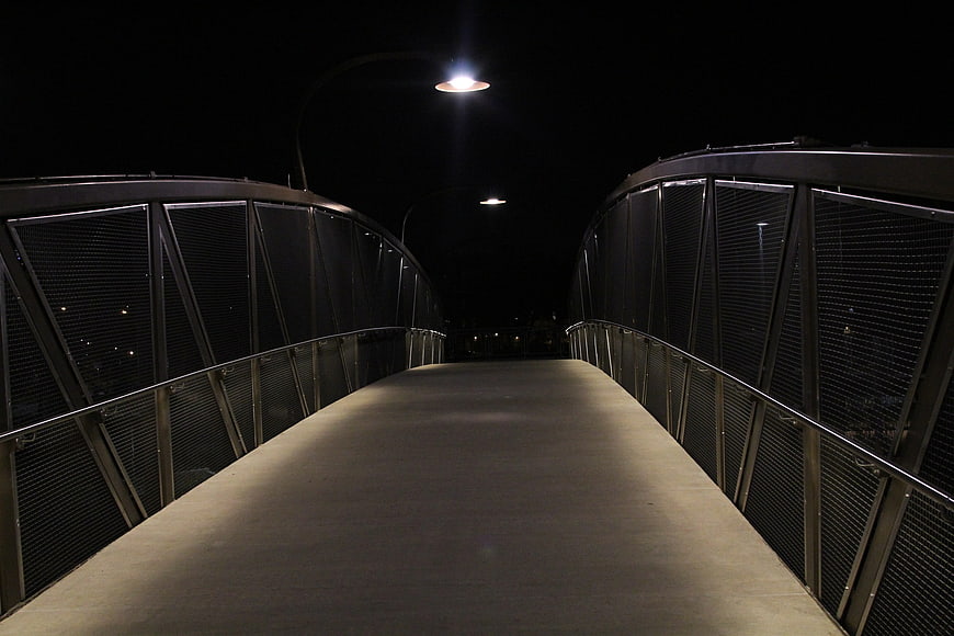 Empty modern pedestrian bridge at night with streetlights