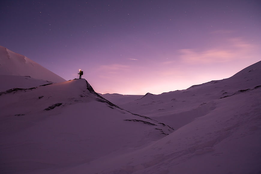 Lone Hiker with Headlamp on Snowy Mountain Ridge at Twilight