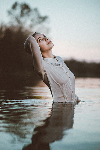 Woman in white shirt standing in water at dusk