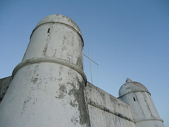 Low angle view of weathered white fortress towers against blue sky