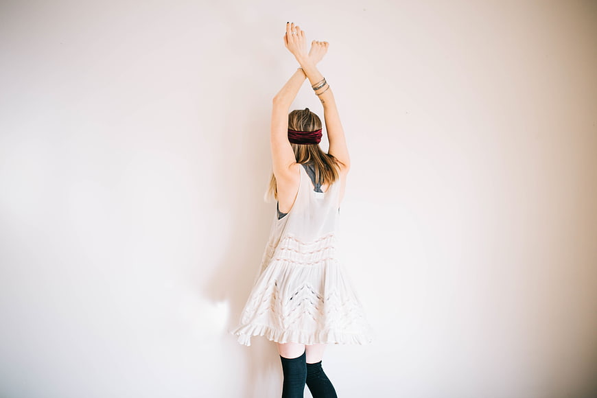 Woman in White Dress with Arms Raised Against White Wall