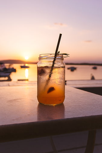 Iced cocktail in mason jar on table at sunset