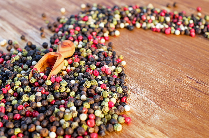 Colorful peppercorns and wooden scoop on rustic wood