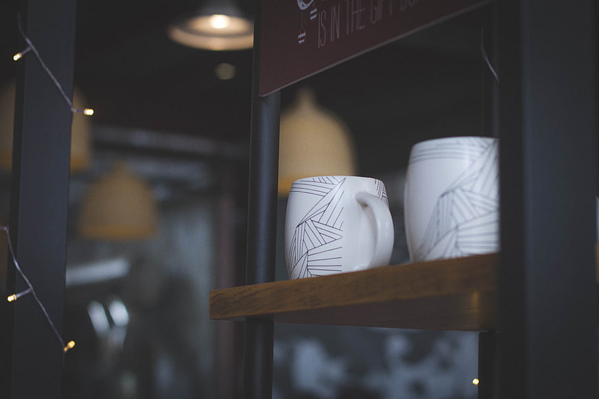 White geometric mugs on wooden shelf in cafe interior