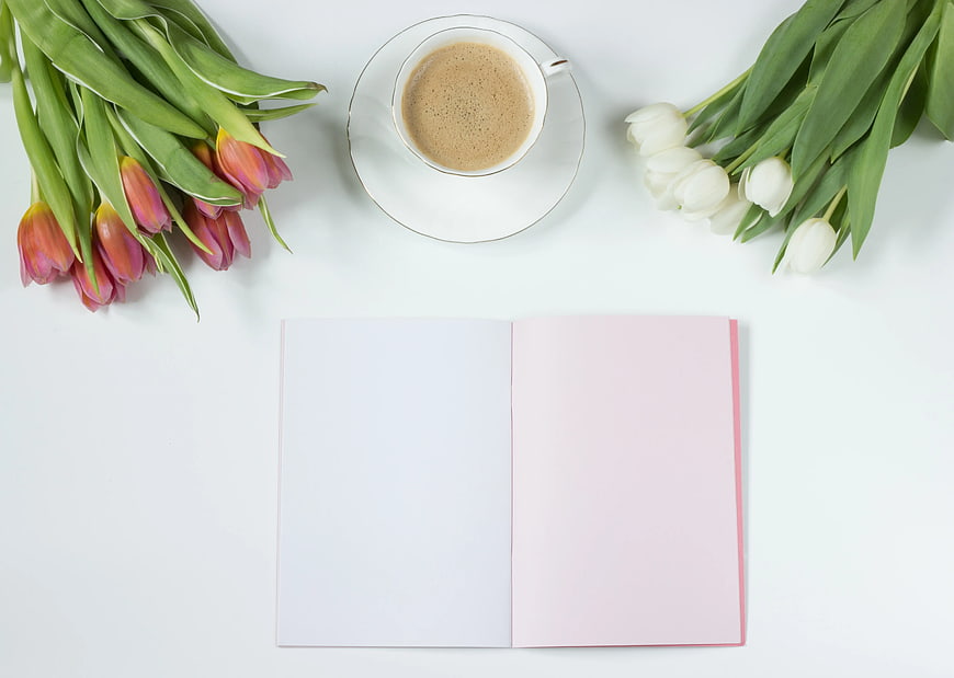 Flat lay of tulips, coffee, and open notebook on white background