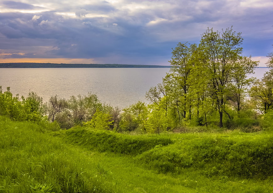 Lush Green Landscape with Lake and Dramatic Cloudy Sky