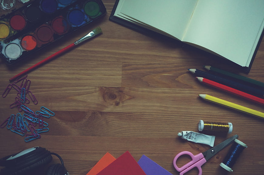 Top-down view of art supplies and notebook on wooden desk