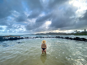 Woman in straw hat standing in ocean water looking at horizon