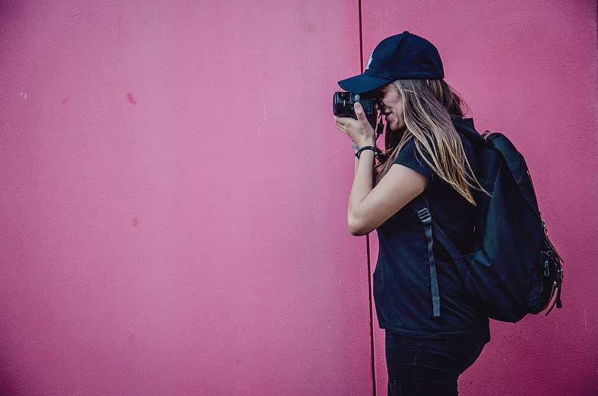 Woman Photographer Taking Photo Against Pink Wall