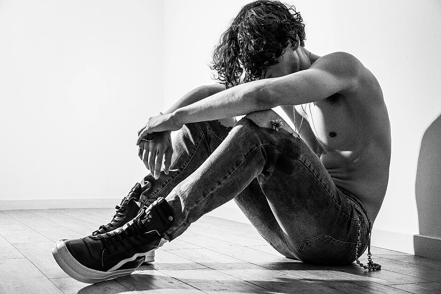 Topless man sitting on floor in black and white