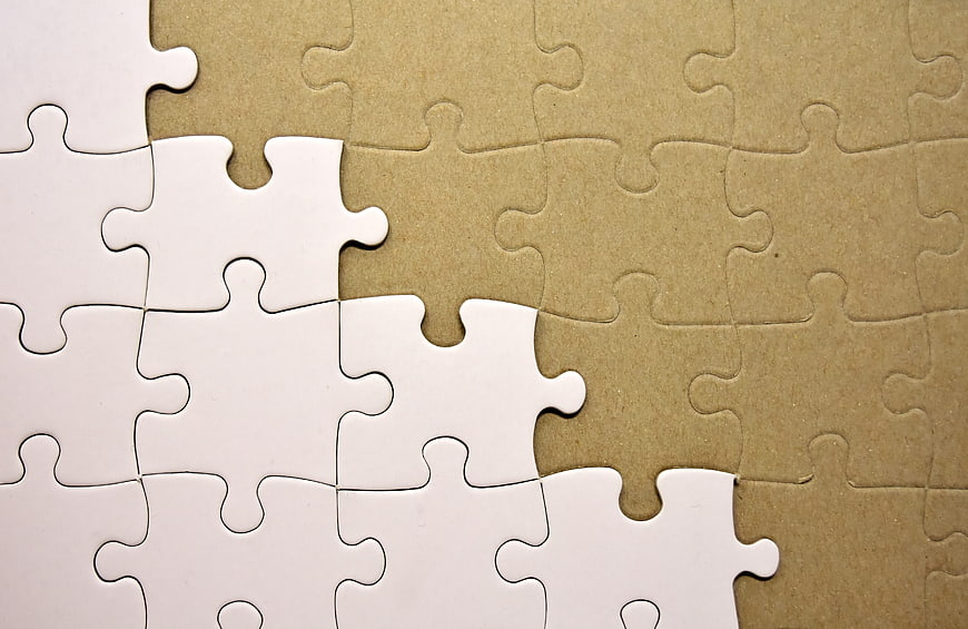 White Jigsaw Puzzle Pieces On Brown Cardboard Background