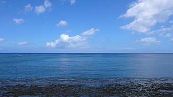 Serene Blue Ocean Horizon with Rocky Shoreline and Clouds