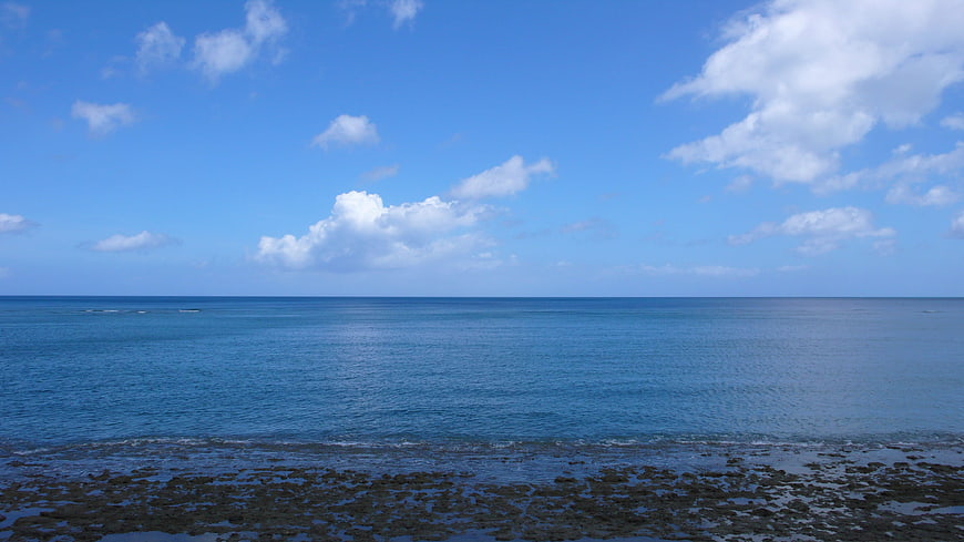 Serene Blue Ocean Horizon with Rocky Shoreline and Clouds