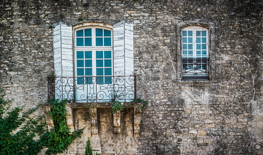 Old stone building facade with blue shutters and balcony