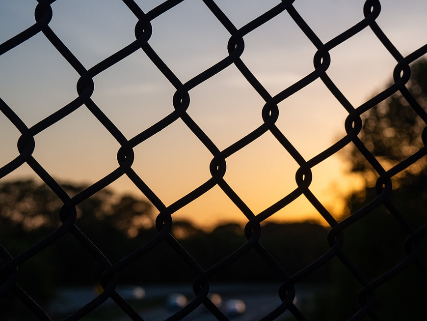 Chain link fence silhouette against golden sunset sky
