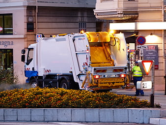White Garbage Truck Operating On Urban Street At Dusk