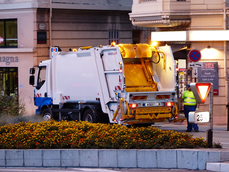 White Garbage Truck Operating On Urban Street At Dusk