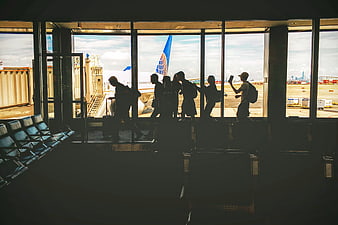 Silhouettes of travelers walking past airport terminal windows